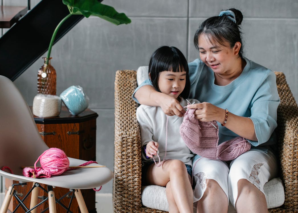 Free Loving Asian grandmother teaching little charming girl to knit spending time together at home Stock Photo