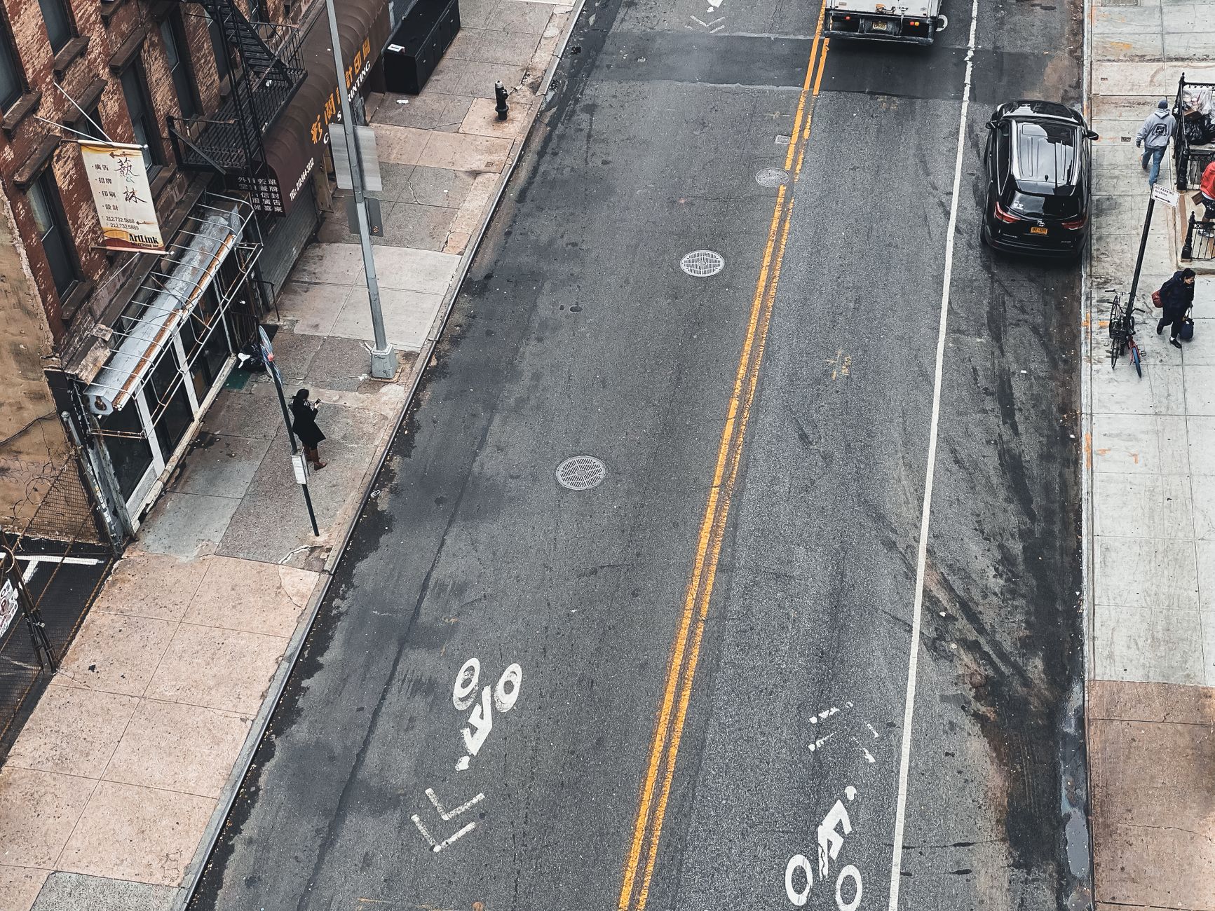 A high-angle view of a city street with a marked bike lane and pedestrians.