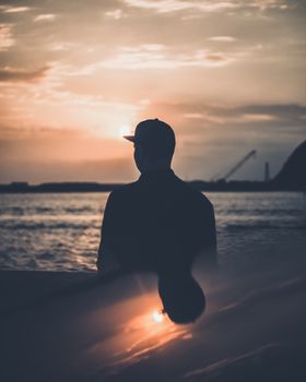 一个戴着帽子的男人剪影，站在宁静日落时的大海边