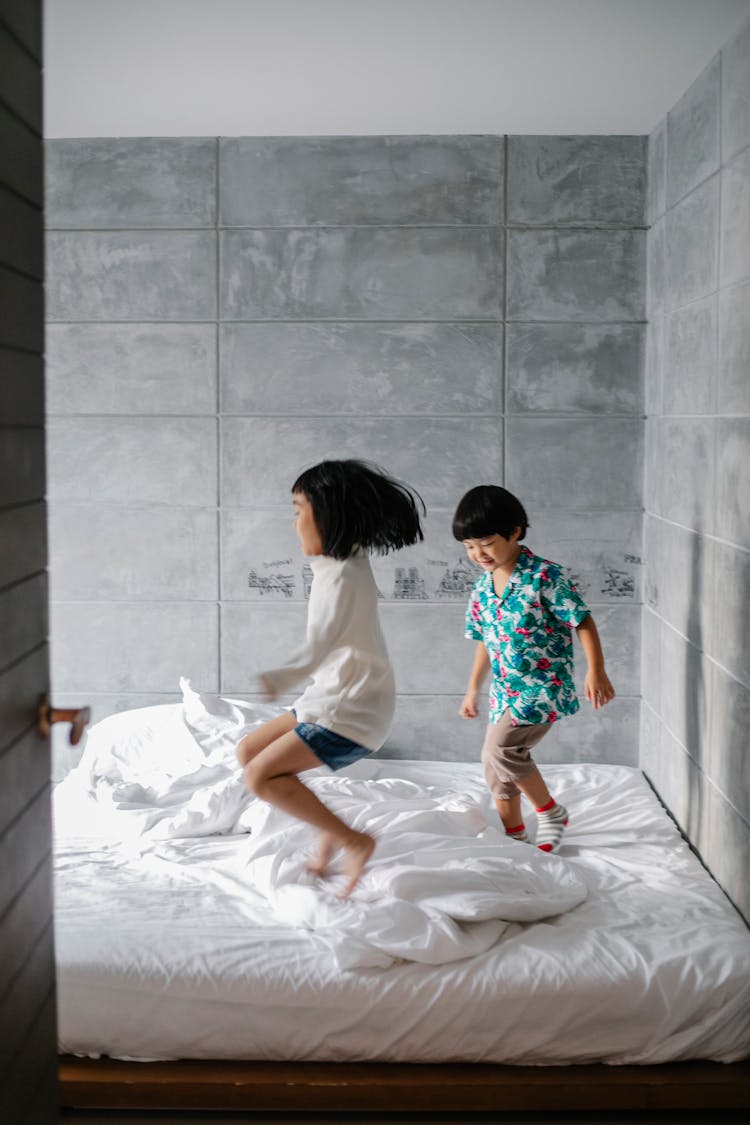 Happy Little Ethnic Siblings Jumping On Bed At Home