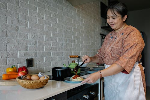 Contenuto Senior Donna Etnica Cucinare Appetitosi Spaghetti Con Salsa In Piedi Al Tavolo Con Verdure Fresche E Uova In Cucina