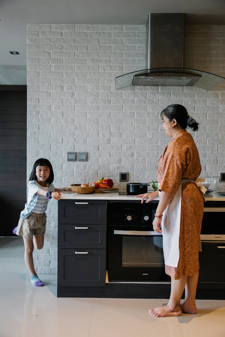 Happy Asian Grandmother With Little Girl Standing In Kitchen In Stylish House