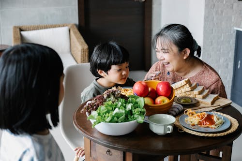 Happy aged Asian woman with grandchildren having tasty breakfast at home