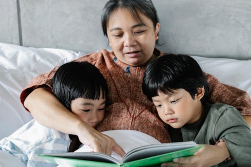 Free Ethnic mother and little kids reading book in bed Stock Photo