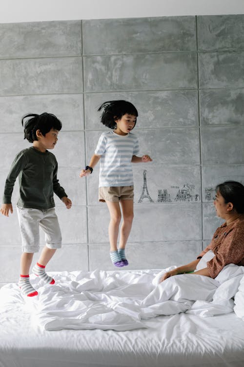 Ethnic siblings jumping on bed in bedroom