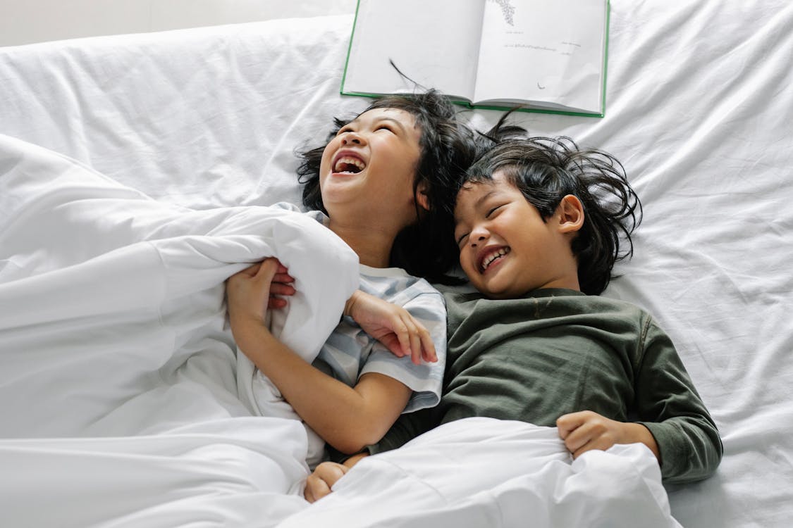 Ethnic kids laughing while lying in bed