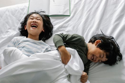 晨光下，两个快乐的孩子一起在舒适的床上欢笑