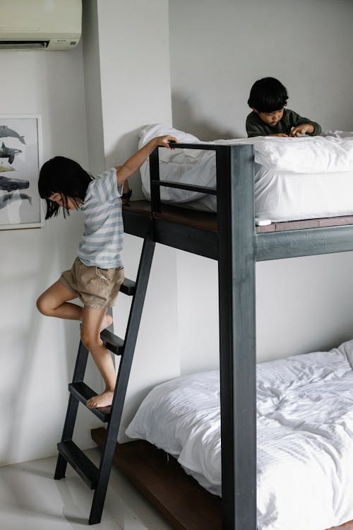 Free Asian girl getting down stair of bunk bed in bedroom with boy sitting on bed in morning in light apartment Stock Photo