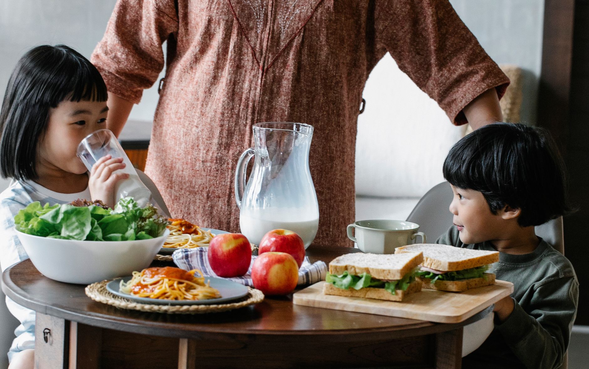 Children enjoying a nutritious breakfast with milk, sandwiches, and salad at the family table.