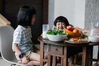 早餐时间，愉快的亚洲男孩和女孩坐在厨房的餐桌旁，桌上摆着一碗水果和一壶牛奶
