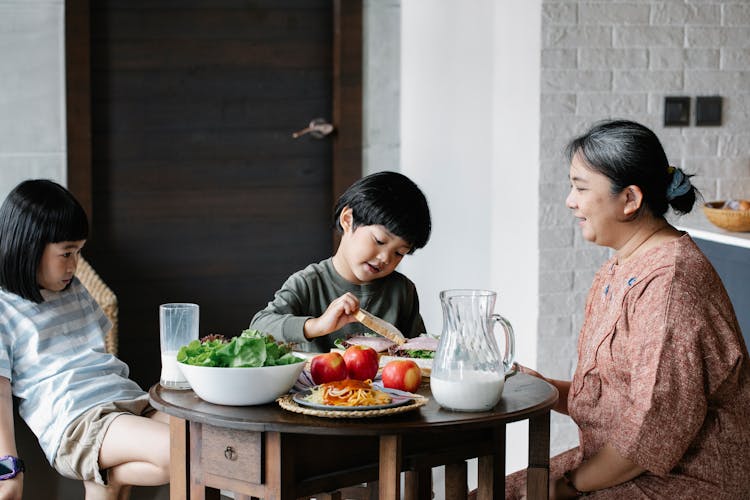 Asian Grandmother Feeding Children In Kitchen