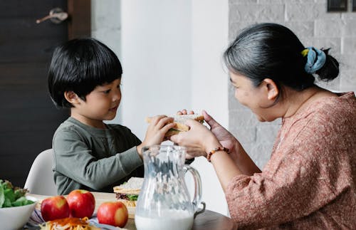 Grandmother giving sandwich to Asian grandson