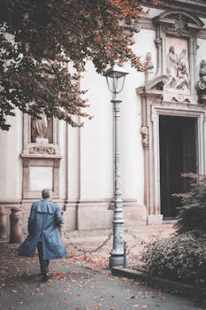 一名身穿蓝色外套的孤独男子沿着米兰的一座历史建筑行走，捕捉秋天的精髓
