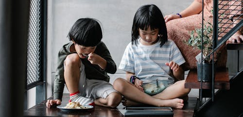 Asian children watching video on tablet and having snack at home