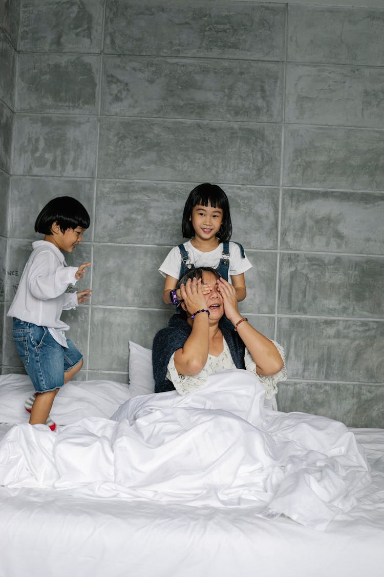 Excited Ethnic Kids Having Fun With Grandmother On Soft Bed