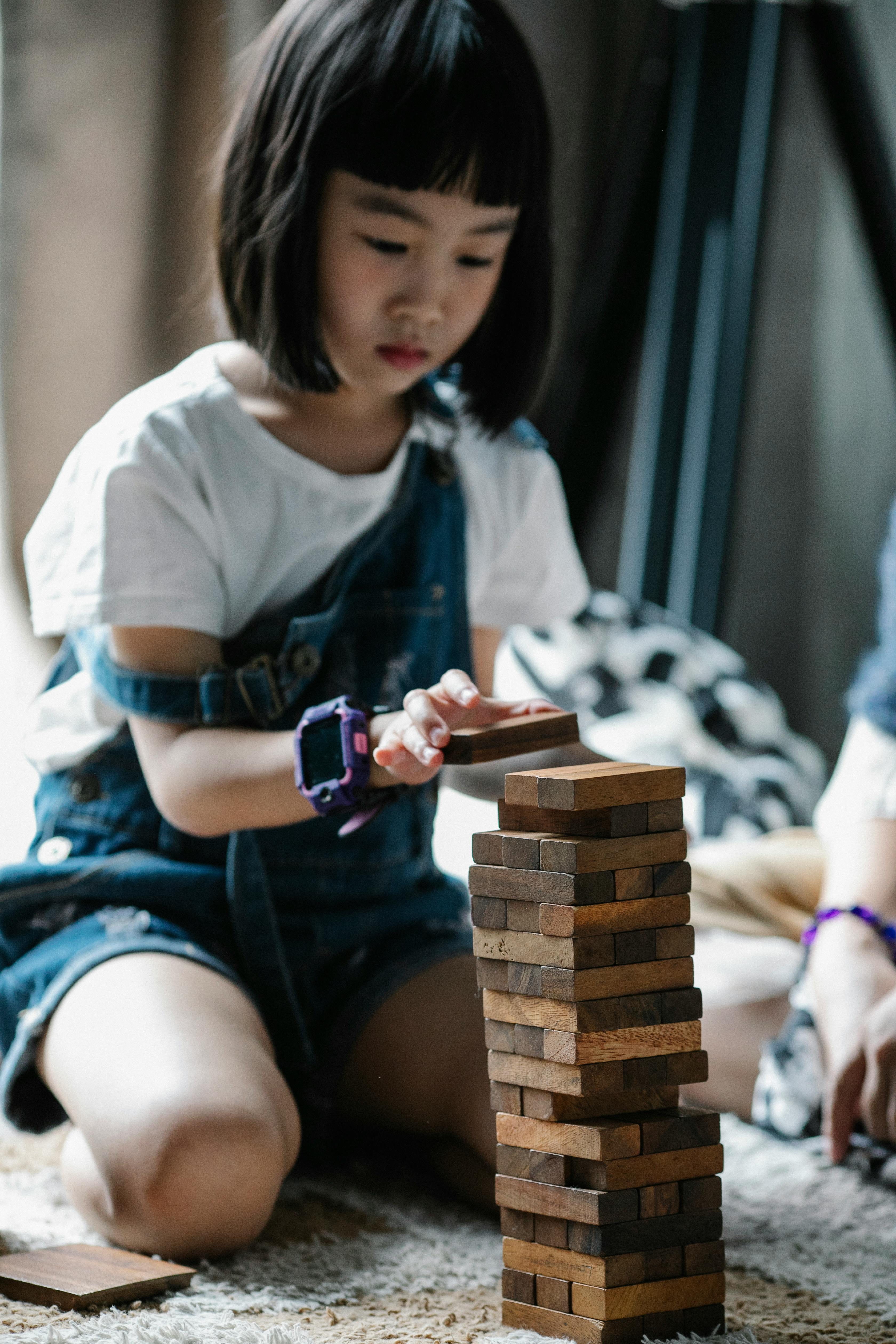 serious asian child playing with tower game sitting on carpet