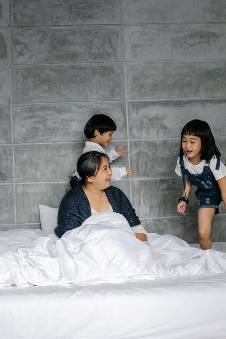 Active Children Running On Bed Around Sitting Grandmother