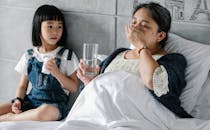 Ill ethnic woman taking medicine while lying in bed near adorable granddaughter