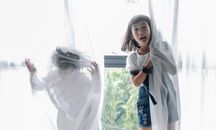 Funny ethnic children hiding behind curtain while playing together at home