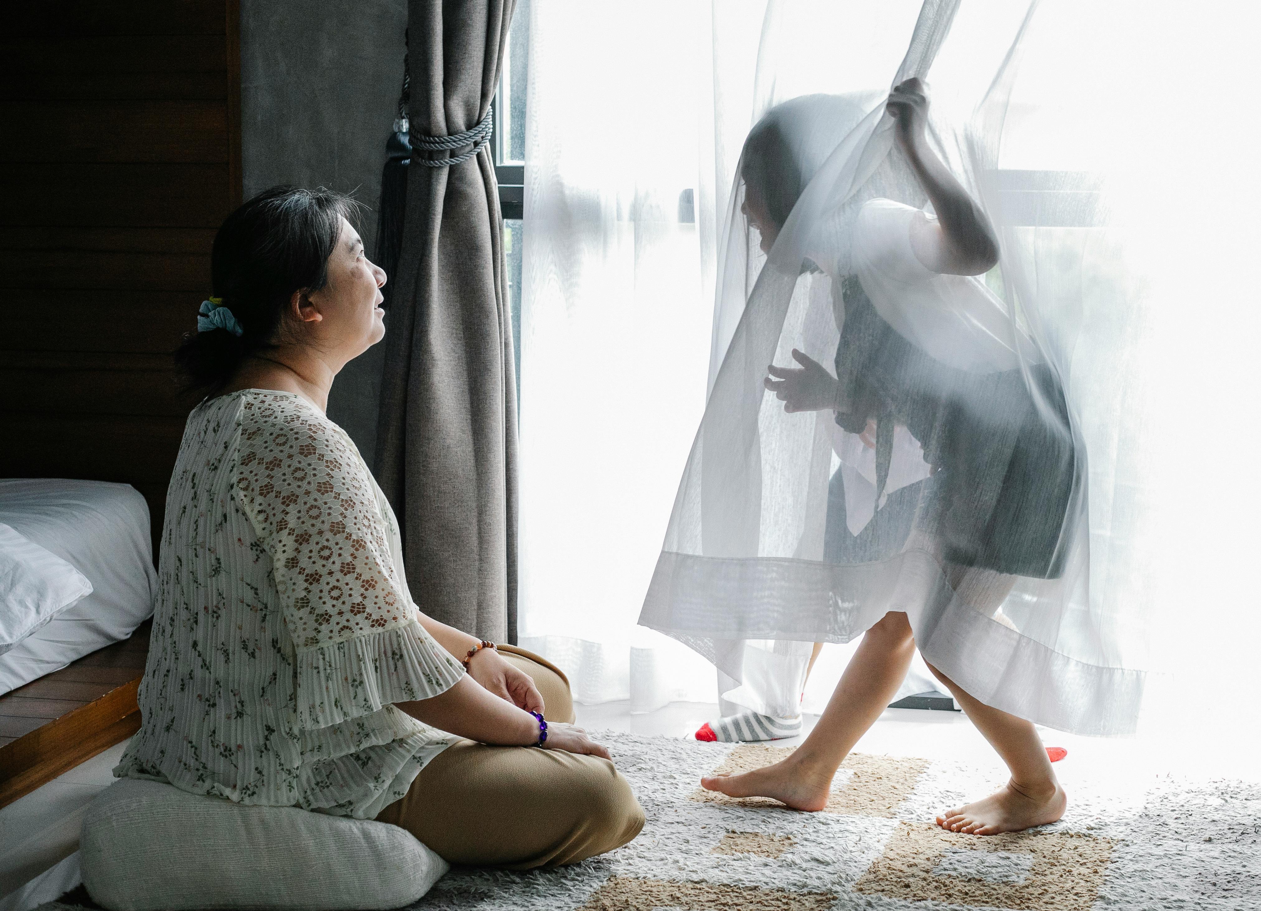 anonymous little girl having fun with asian grandmother sitting on floor in bedroom