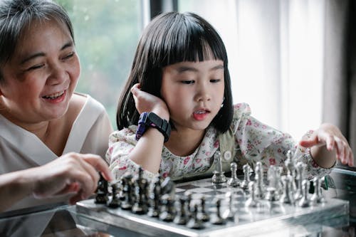 Adorable ethnic child doing move while playing chess with grandmother