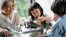 一位年长的少数族裔女性在明亮的房间里，愉快地帮助可爱的小孙子在桌子上下棋