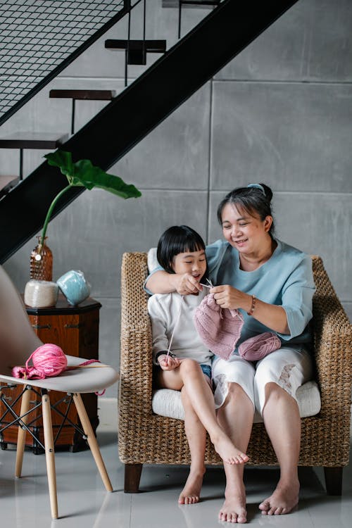 Free Positive woman teaching adorable child to knit with needles at home Stock Photo