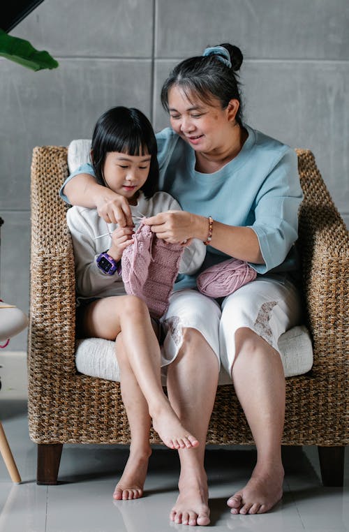 Joyful Asian kid knitting warm clothes with kind grandmother