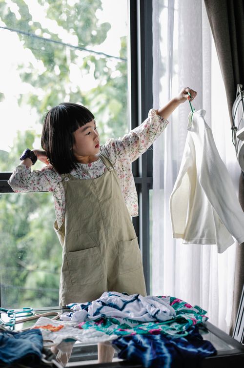 Free Cute little stylish Asian girl standing in room near window and hanging clothes into wardrobe Stock Photo