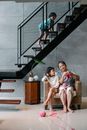 Ethnic kid playing on stairs near grandmother and sister knitting at home
