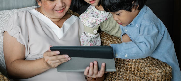 Anonymous Asian Woman With Grandchildren Watching Video On Tablet