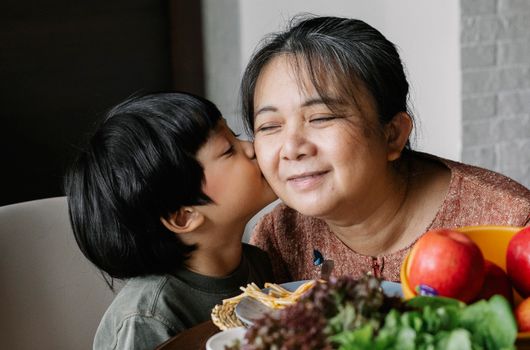 一位快乐的少数族裔妇女坐在餐桌旁，微笑着抚摸孙子，吃着各种新鲜水果