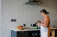 Side view of elderly female in apron standing near stove and holding pan while preparing lunch at home