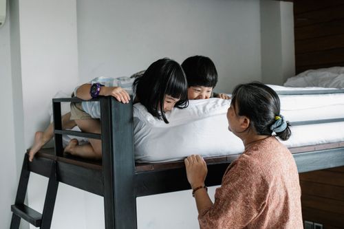 Free Faceless grandmother standing near bunk beds while Asian kids hiding and having fun on mattress Stock Photo