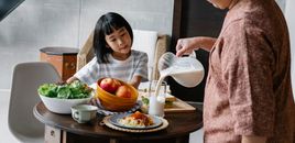 一位亚洲母亲站在桌旁，为家里可爱的孩子准备健康午餐