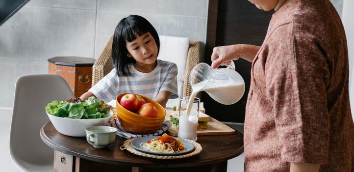 一位亚洲母亲站在桌旁，为家里可爱的孩子准备健康午餐