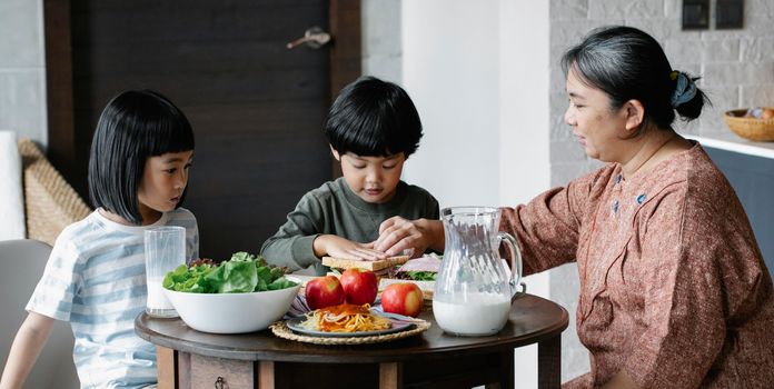 祖母和两个孩子坐在摆满新鲜食物的桌子旁吃饭