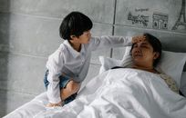 Little Asian boy measuring temperature of sleeping grandmother
