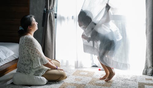 Free Full length of Asian woman sitting on floor with crossed legs and enjoying time with children covering face with curtain Stock Photo
