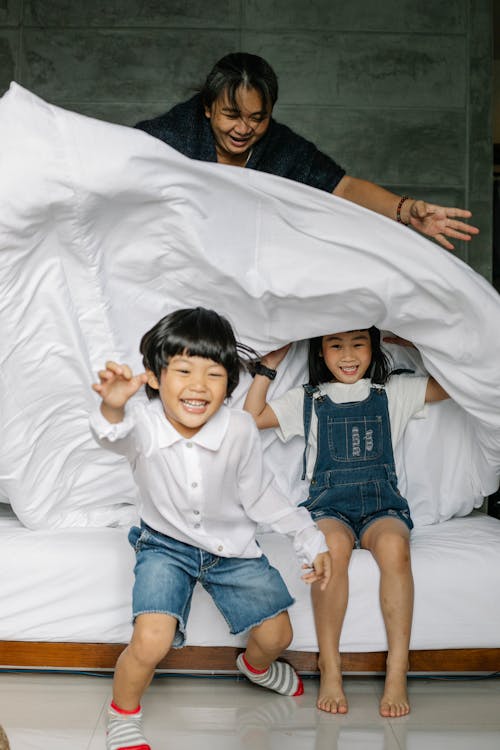 Full length of Asian children in casual clothes toothy smiling while playing with grandmother in bedroom