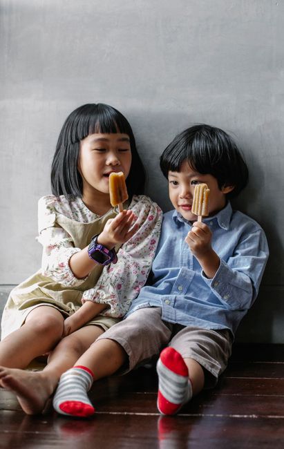 Content Asian kids in casual clothes sitting on floor and enjoying yummy ice creams together