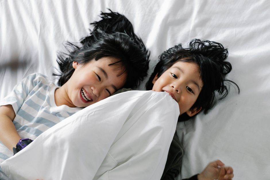 Two happy Asian children enjoying playful time together on bed indoors.