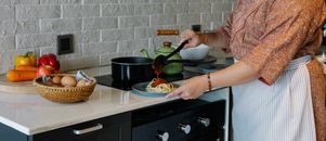 Side view crop housewife in apron cooking lunch in kitchen and adding fresh delicious tomato sauce to Italian pasta