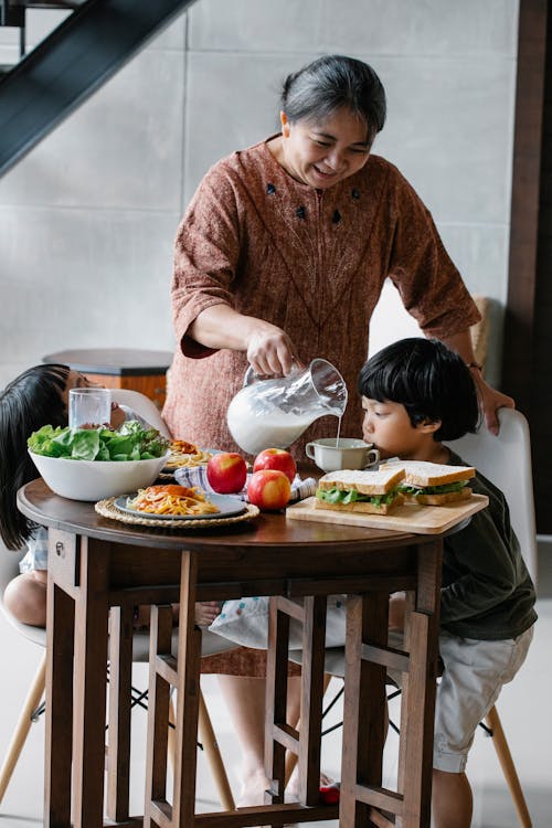 孫のためにカップに牛乳を注ぐアジアの祖母