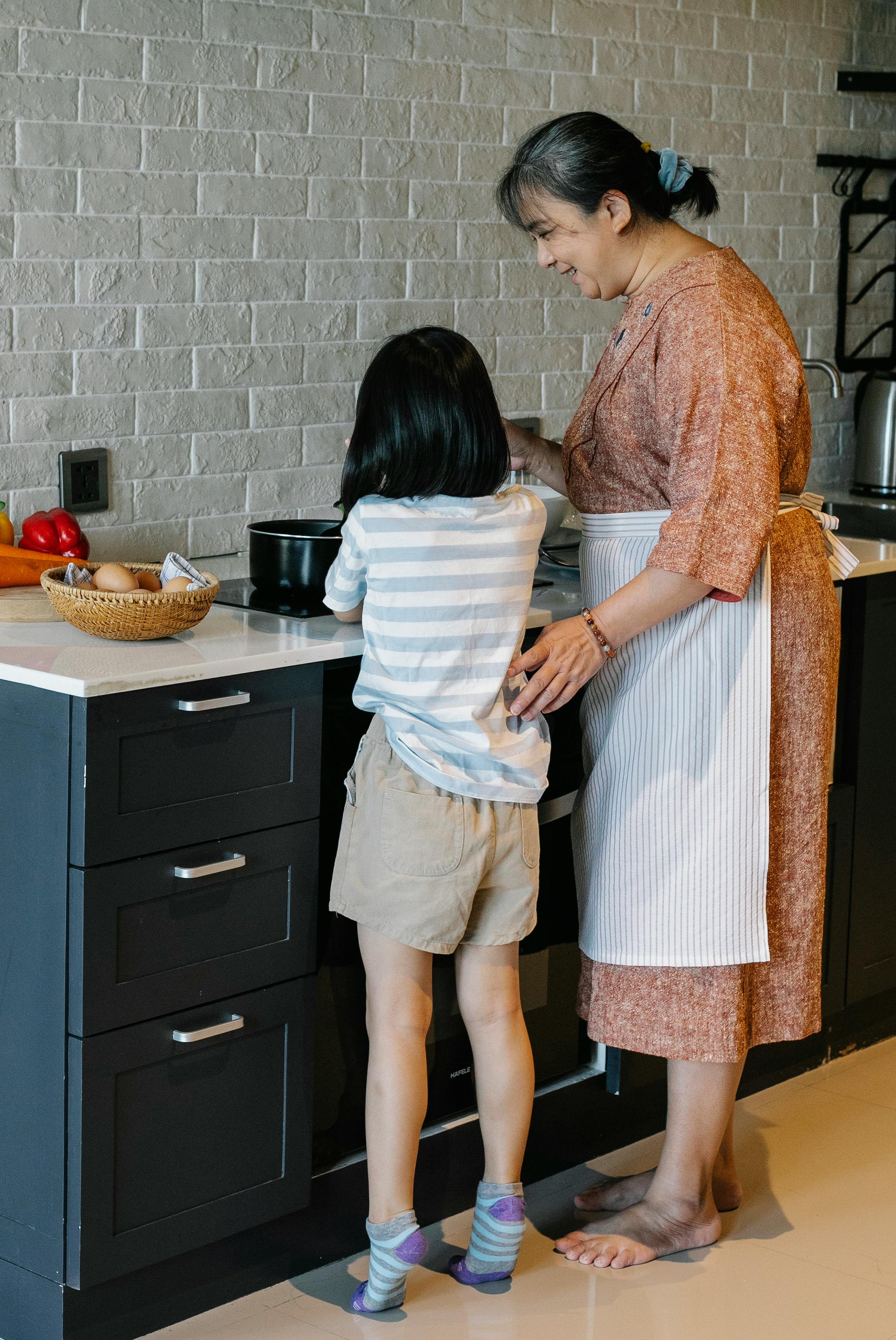 smiling asian grandmother teaching little granddaughter to cook