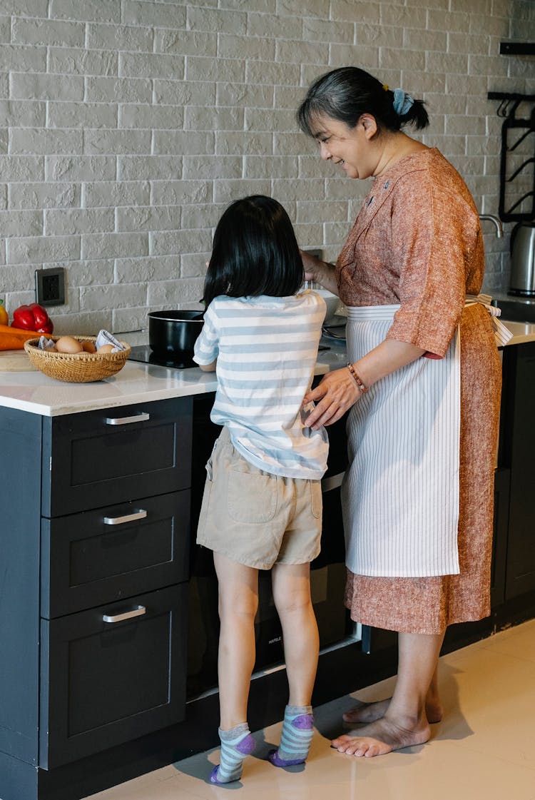 Smiling Asian Grandmother Teaching Little Granddaughter To Cook