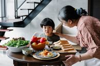 Adorable Asian boy eating pasta near attentive granny in kitchen
