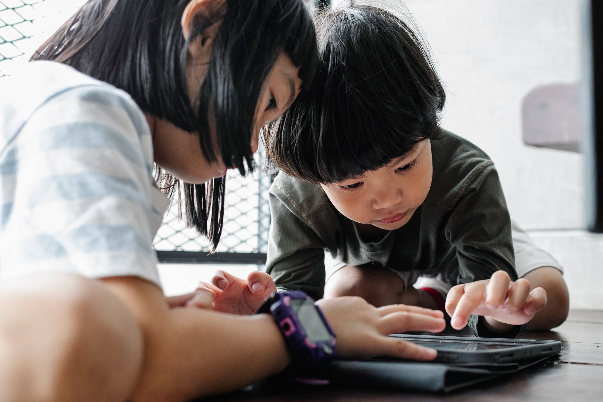 Two children closely focused on a tablet screen together indoors