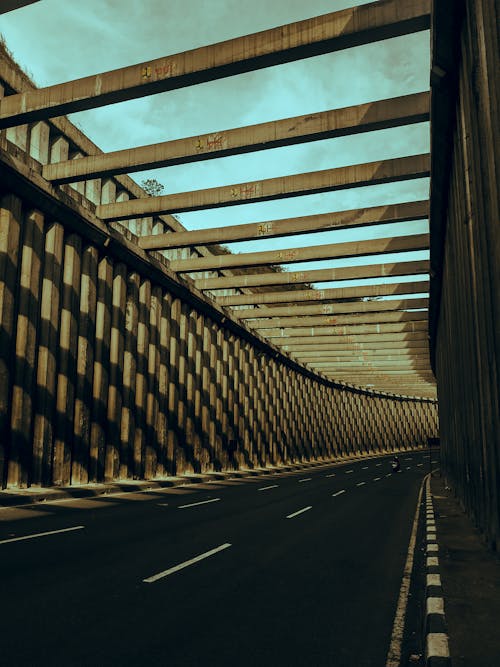 Asphalt roadway between geometric cement fence under beams and sky with clouds in town