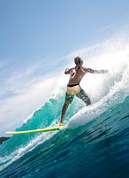 Back view of faceless muscular young male surfer in swimwear riding splashing waves in turquoise ocean during summer holidays on sunny day